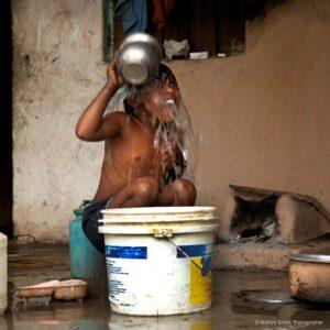 A young boy in Janta Colony take a bucket bath outside.