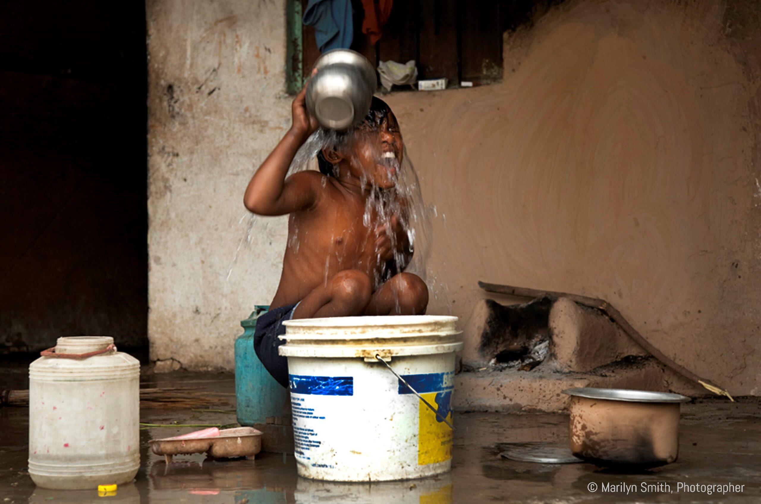 A young boy in Janta Colony take a bucket bath outside.