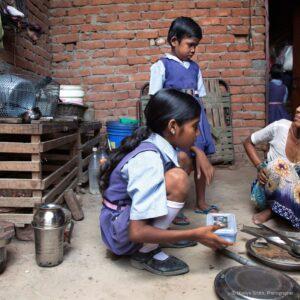 A mother cooking breakfast over an open fire outside their door.