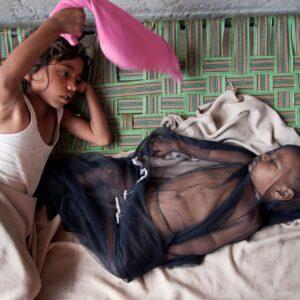 A young girl swatting flies while her baby brother sleeps.