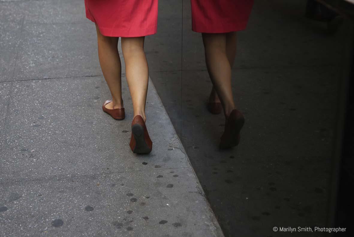 A woman's legs and their reflection in the polished granite of a high-rise in New York City.
