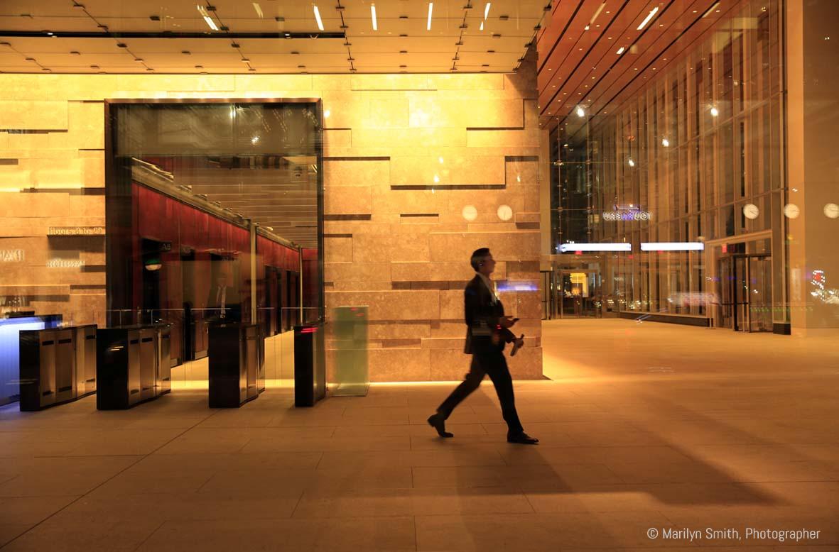 Man walking alone out of a massive office building at night in New York City.
