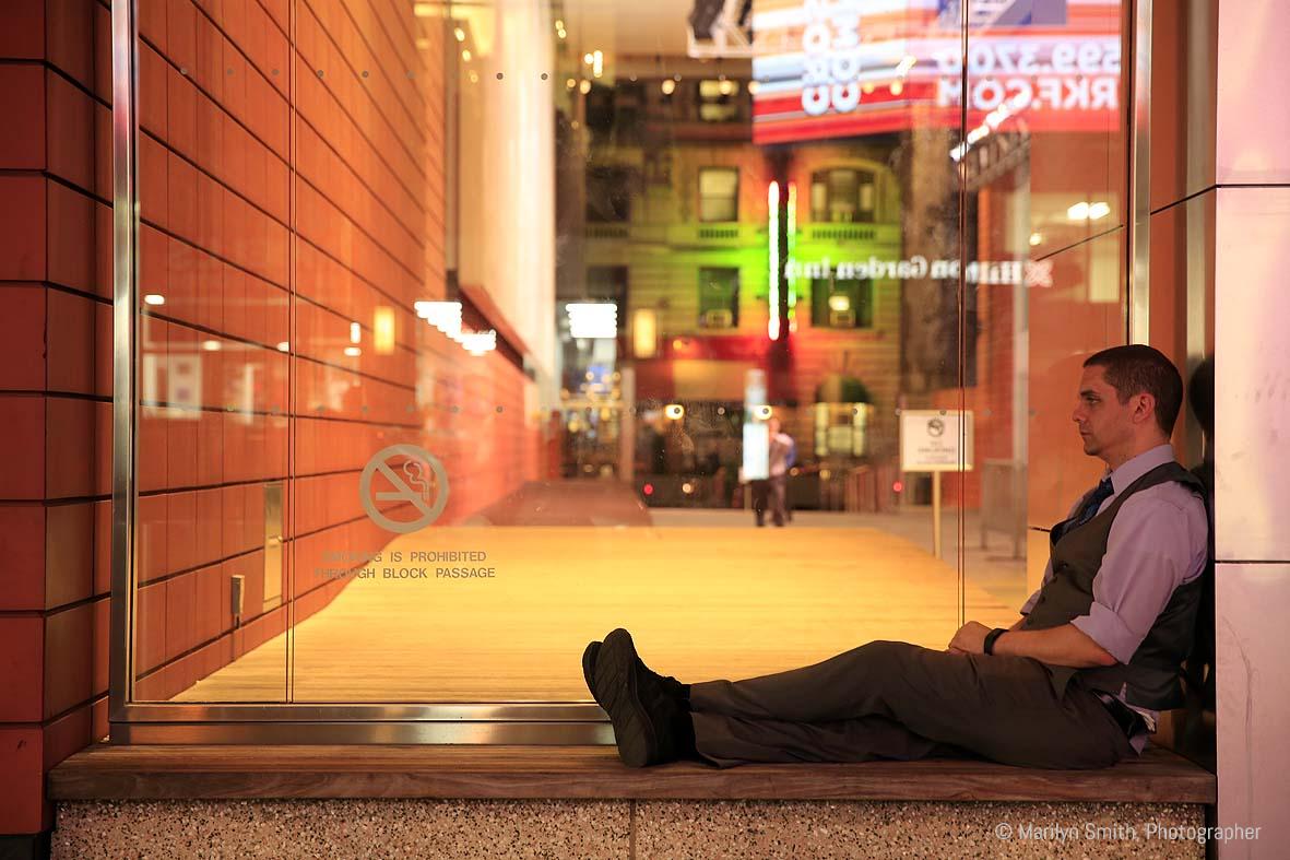 A man taking sitting alone in an office tower building as crowds rush by in New York City.