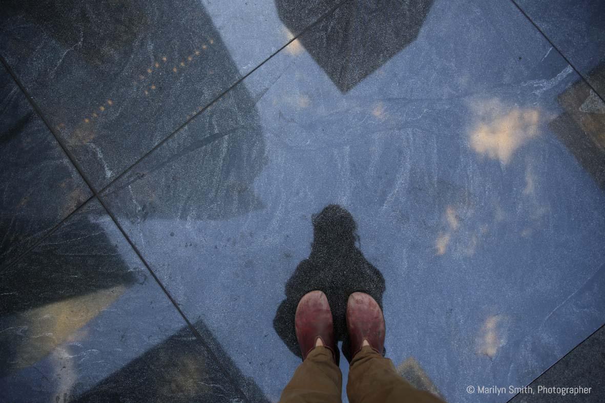 My feet on polished granite reflecting skyscrapers and the sky, New York City.